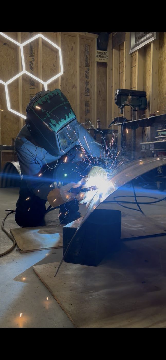 Welder striking an arc, sparks falling and honeycomb shop lights overhead